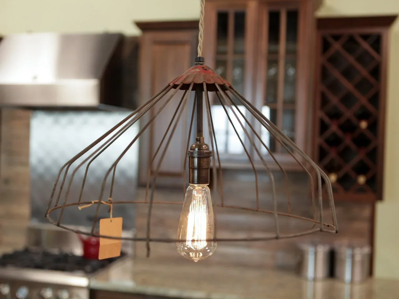 An open metal pendant shade hangs in front of timber kitchen cabinets and a wood counter.