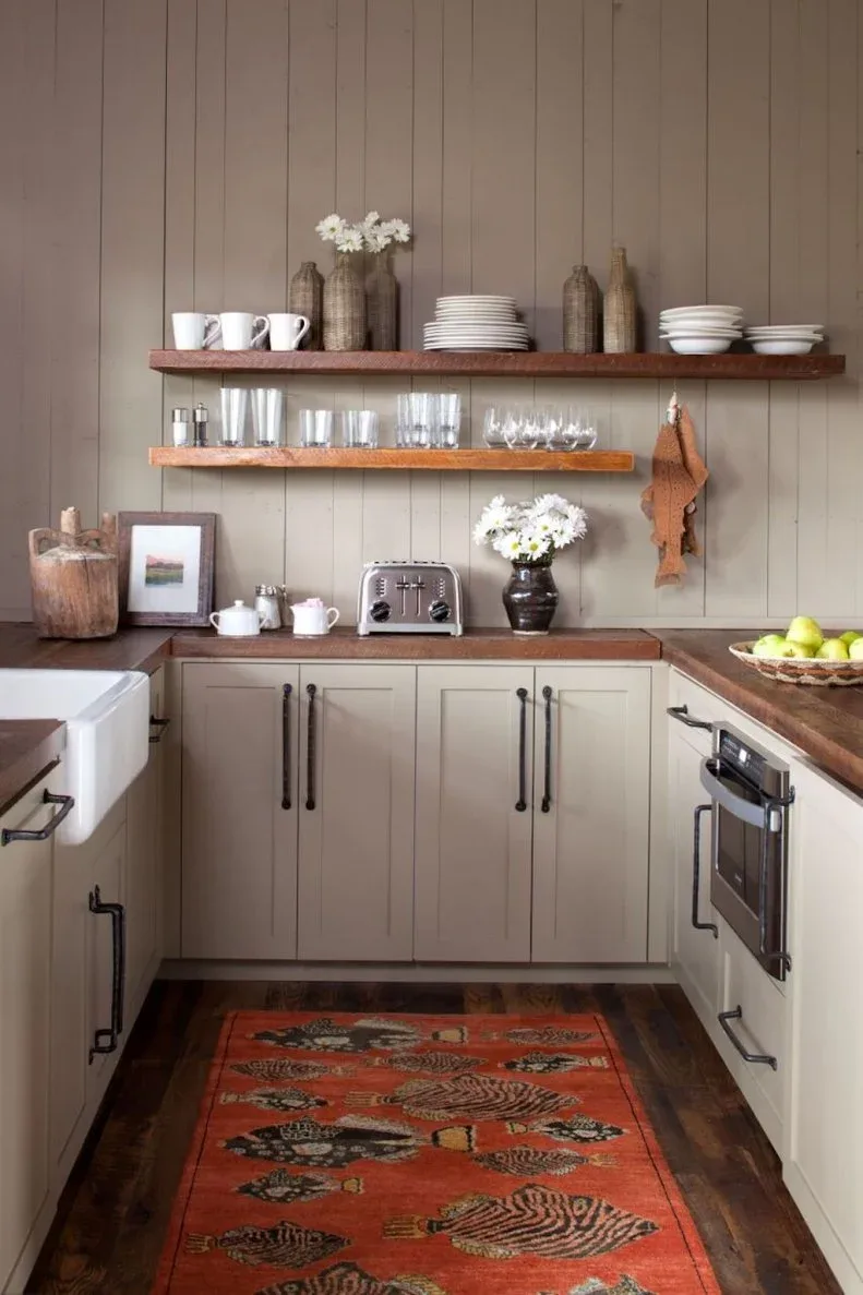 Timber shelves hold white dishes and clear glasses above a wood counter and pale paneled cabinets.