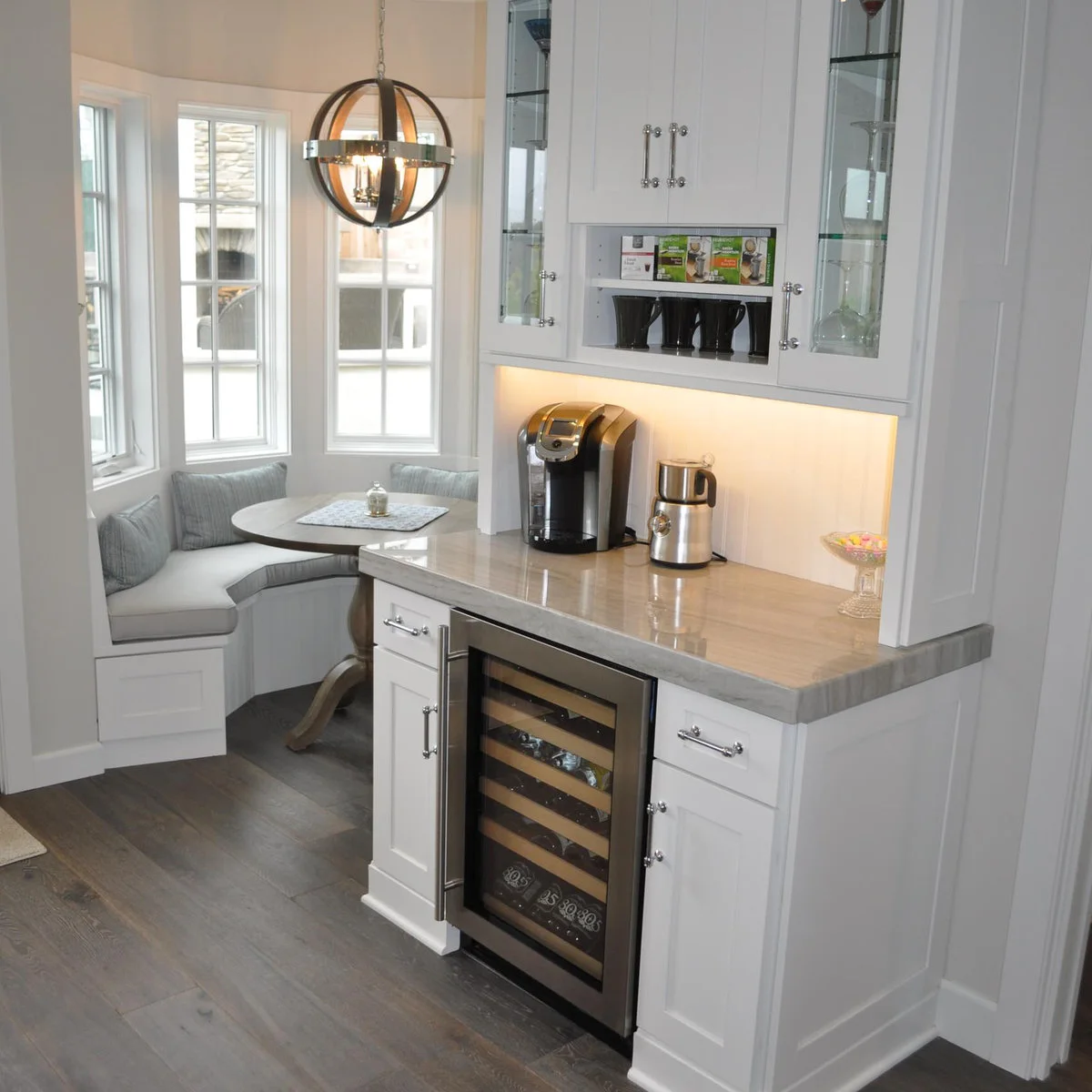 White coffee counter beside a curved breakfast bench with under-cabinet lighting and a small fridge