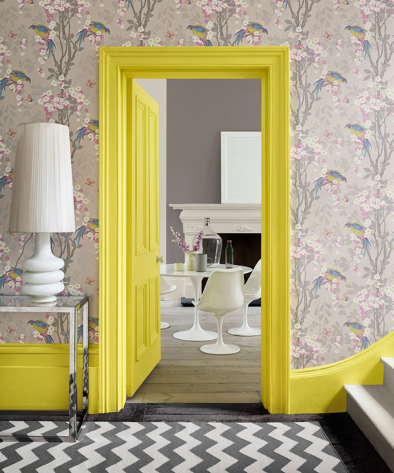 Bright yellow door trim and baseboards surround bird-and-flower wallpaper beside a white lamp and a black-and-white zigzag rug