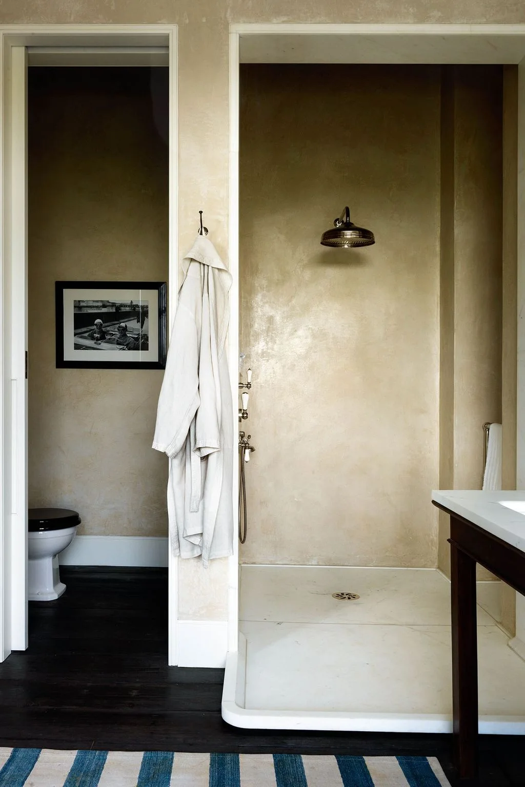 An open shower alcove has pale warm-toned walls, a dark showerhead and a projecting tray with a rounded outer corner.