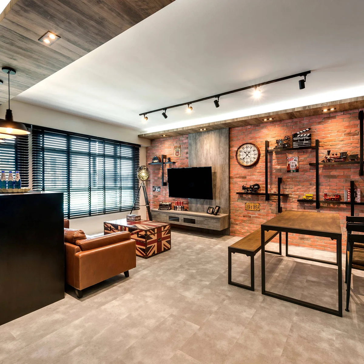 A compact room has a brown sofa facing a wall television, brick-pattern walls and a rectangular dining table with a matching bench to one side.