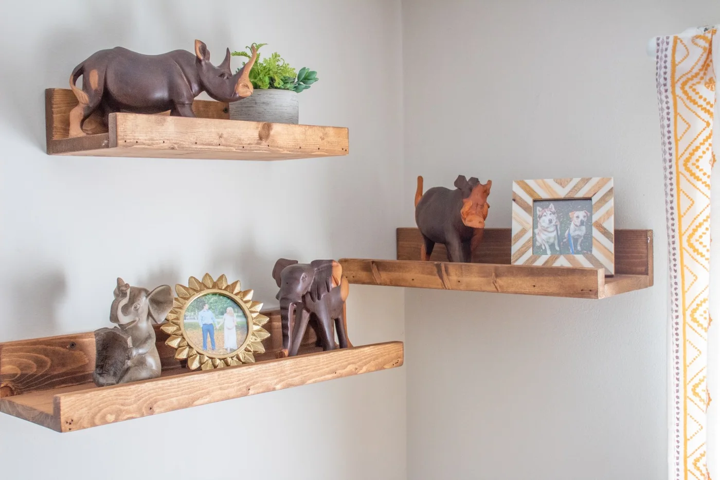 Three timber wall shelves display rhinoceros and elephant figures alongside framed family photographs and a small plant.
