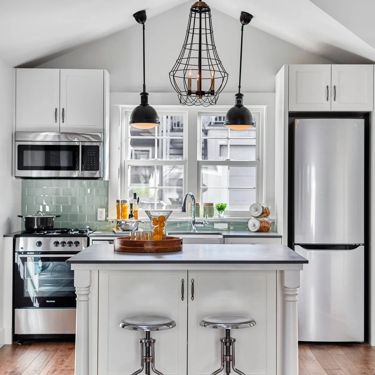 Compact white island with a dark top and two metal stools in a small vaulted kitchen