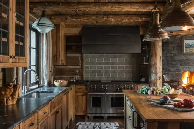 Dark worktops and a substantial hood sit against timber cabinets and exposed logs.
