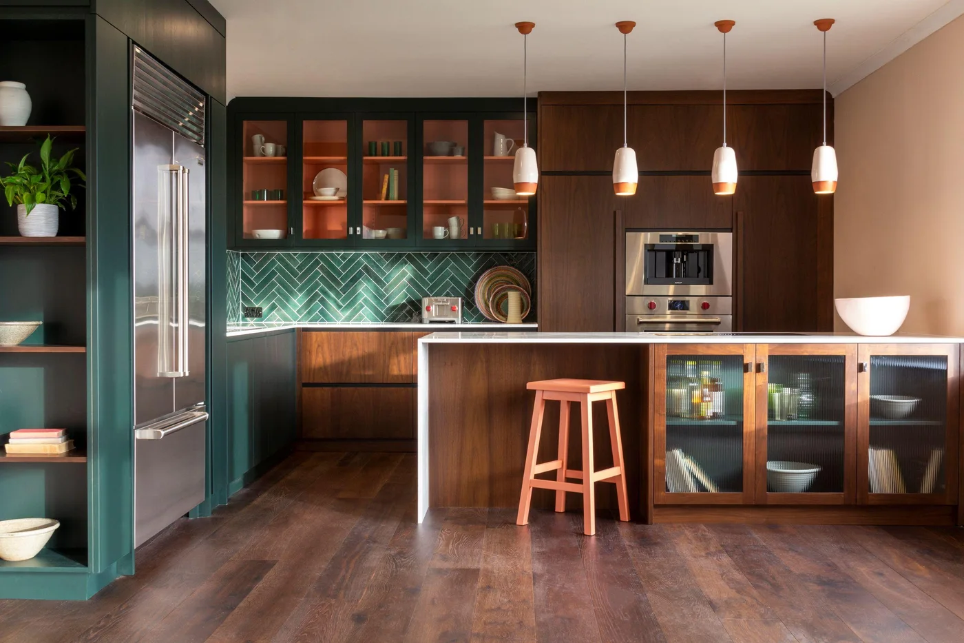 Walnut tall and lower cabinets meet deep green glass-front cupboards with pink interiors and a green herringbone backsplash.
