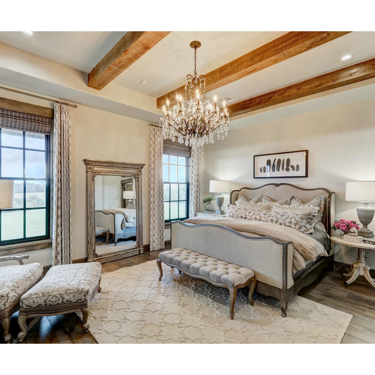 Bedroom with exposed beams, a curved upholstered bed, tufted bench and tall framed mirror