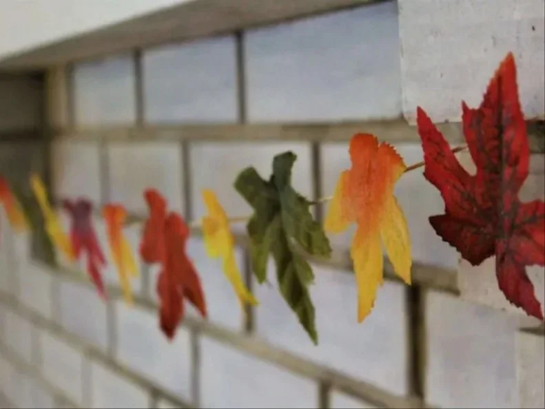 Individual red, orange, yellow and green leaf shapes attach at intervals to a cord against a pale railing