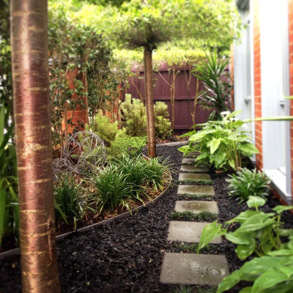 Small rectangular stepping stones curve through dark loose ground cover beside a house