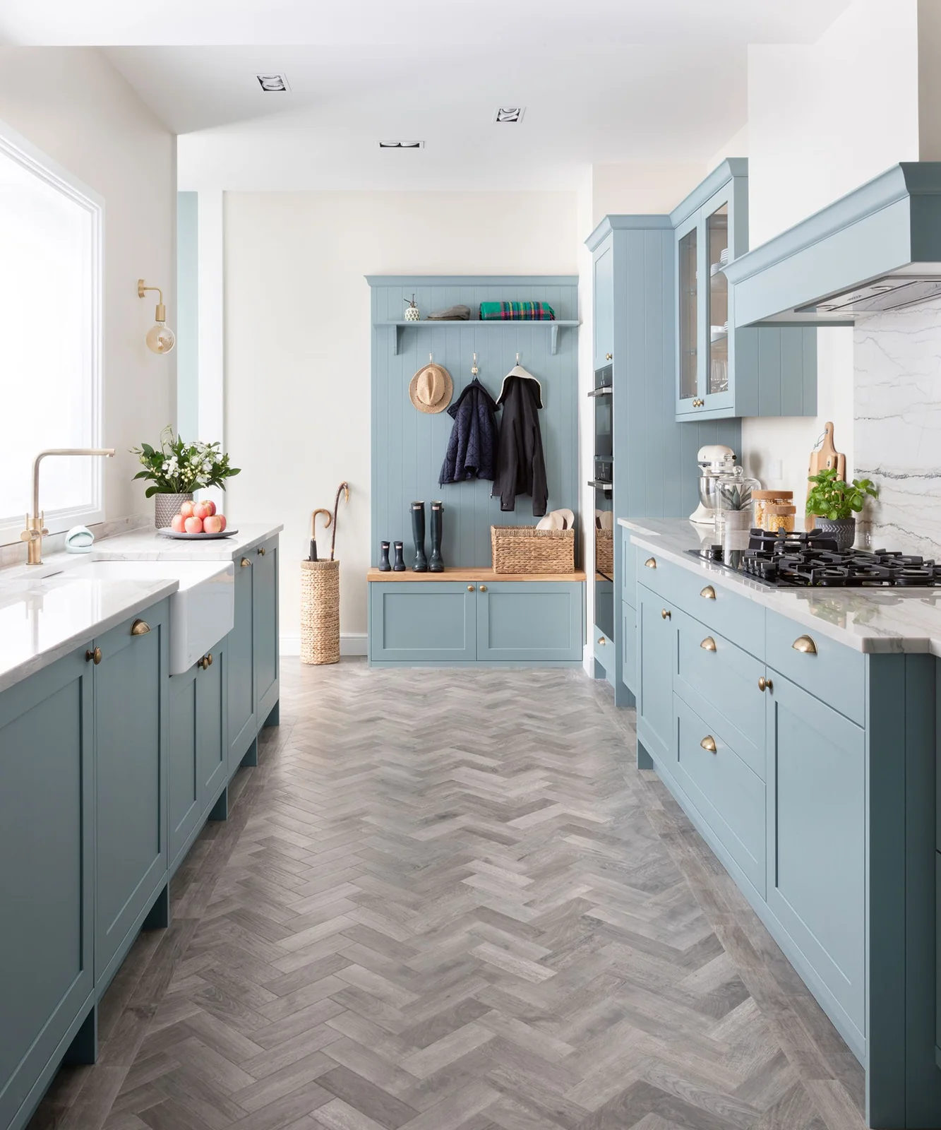 Pale blue galley kitchen with a window-side sink and a matching coat bench at the far end