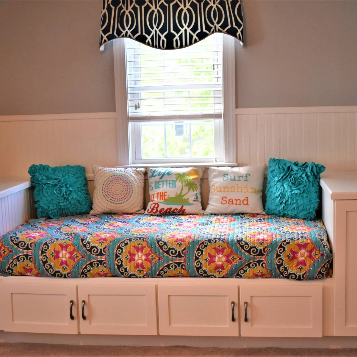 A white built-in daybed with cabinet doors below carries bright patterned bedding and turquoise cushions.