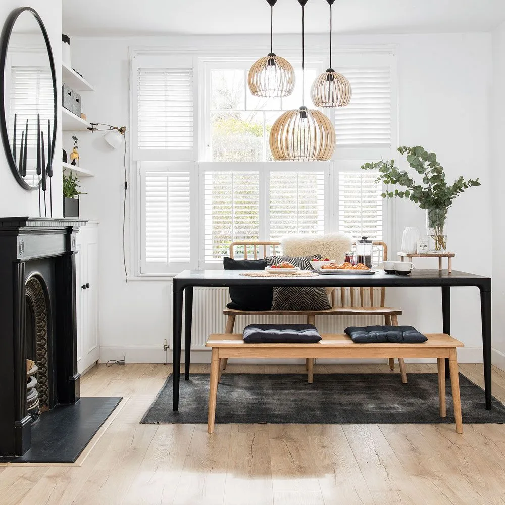 Three open rounded pendants above a dark rectangular dining table with wood benches and white shutters