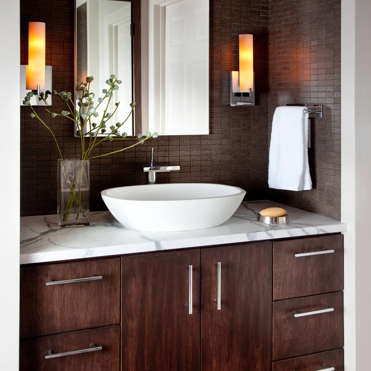 Dark wood vanity with a white vessel basin, green stems in a clear rectangular vase and a soap dish.