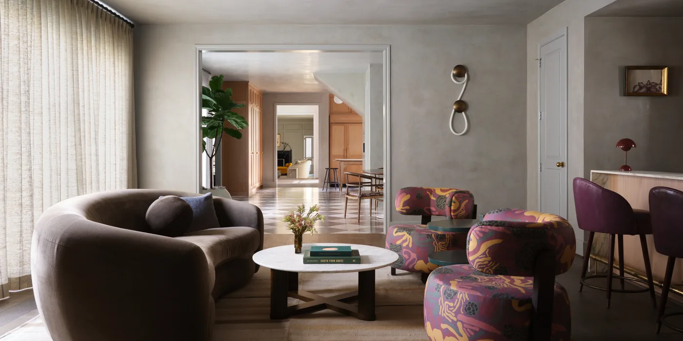 Curved dark brown sofa with purple and yellow patterned chairs around a pale round table.