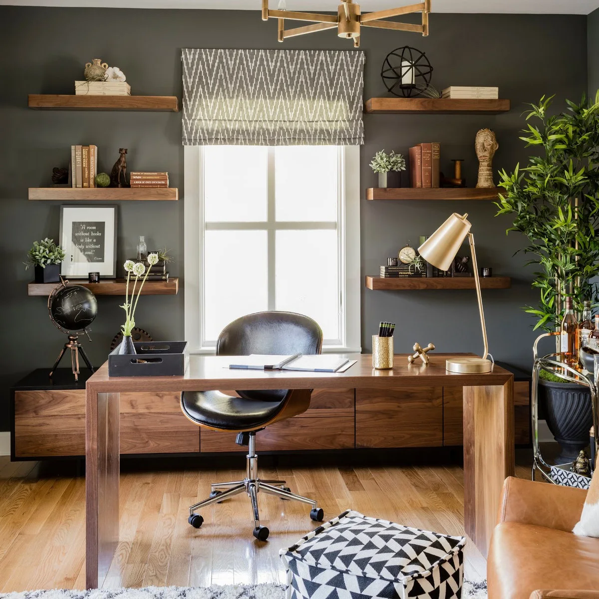 Home office with wood desk, deep gray wall, floating wood shelves and a gold-toned task lamp