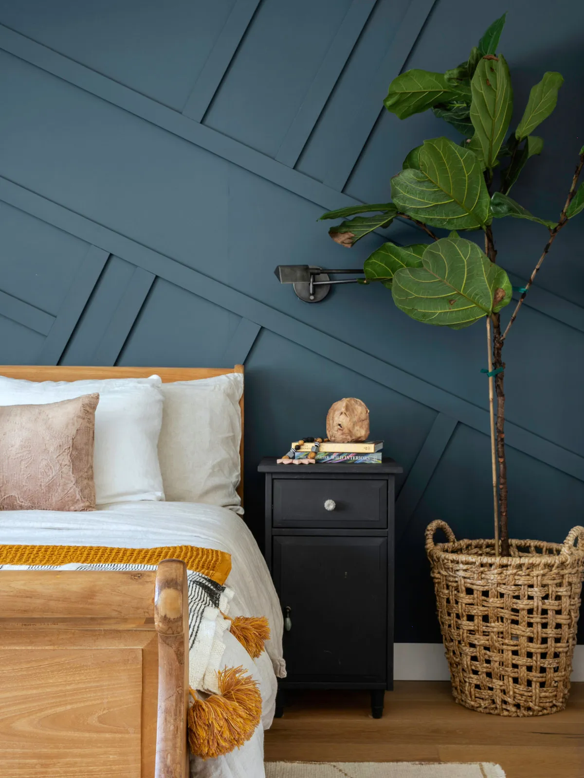 Deep blue diagonal paneling sits behind pale bedding and a timber footboard.