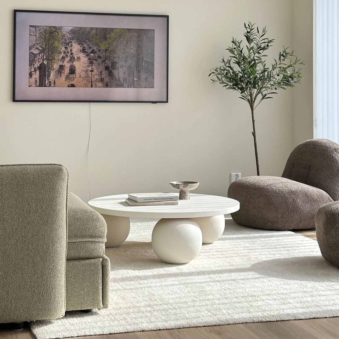 White round coffee table with large spherical supports between neutral upholstered chairs