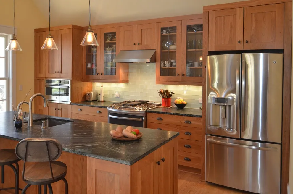 Wood cabinet fronts sit beside a dark island worktop and stainless appliances