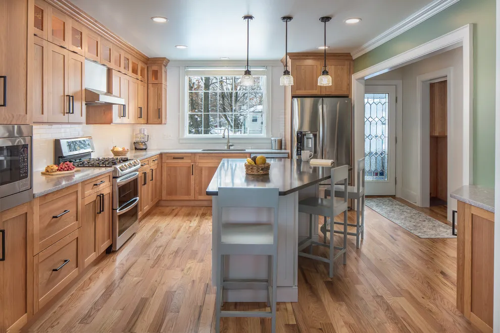 Warm wood cabinets surround a smaller gray island beneath pale pendant lights
