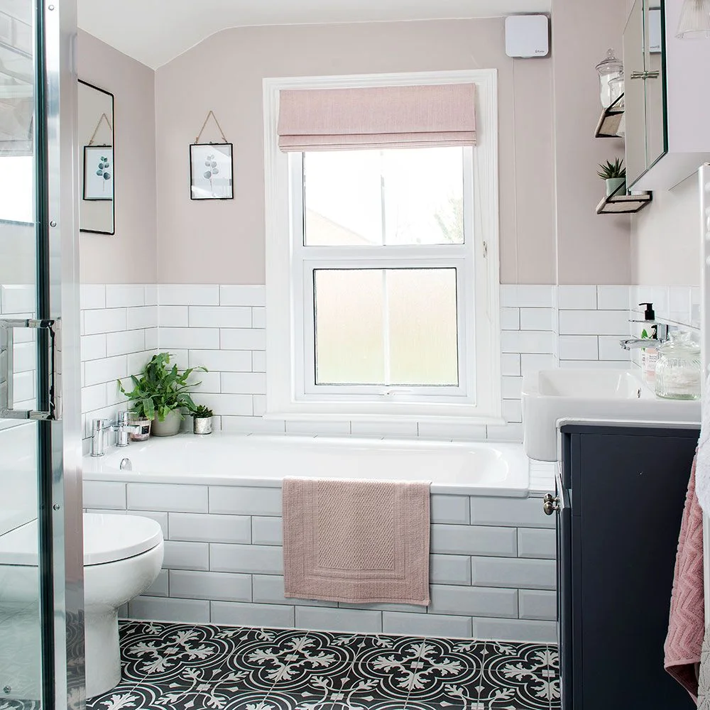 Compact bathroom with plain white subway tile around a fitted bath, pale pink upper wall and dark patterned floor.
