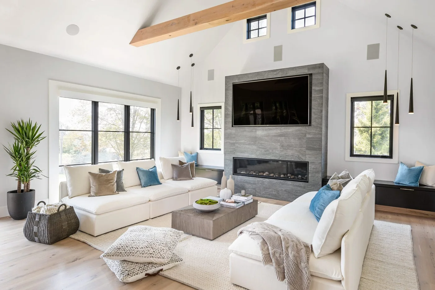 Two pale sofas face a low rectangular table beneath a gray fireplace and television wall, with blue cushions and a light rug