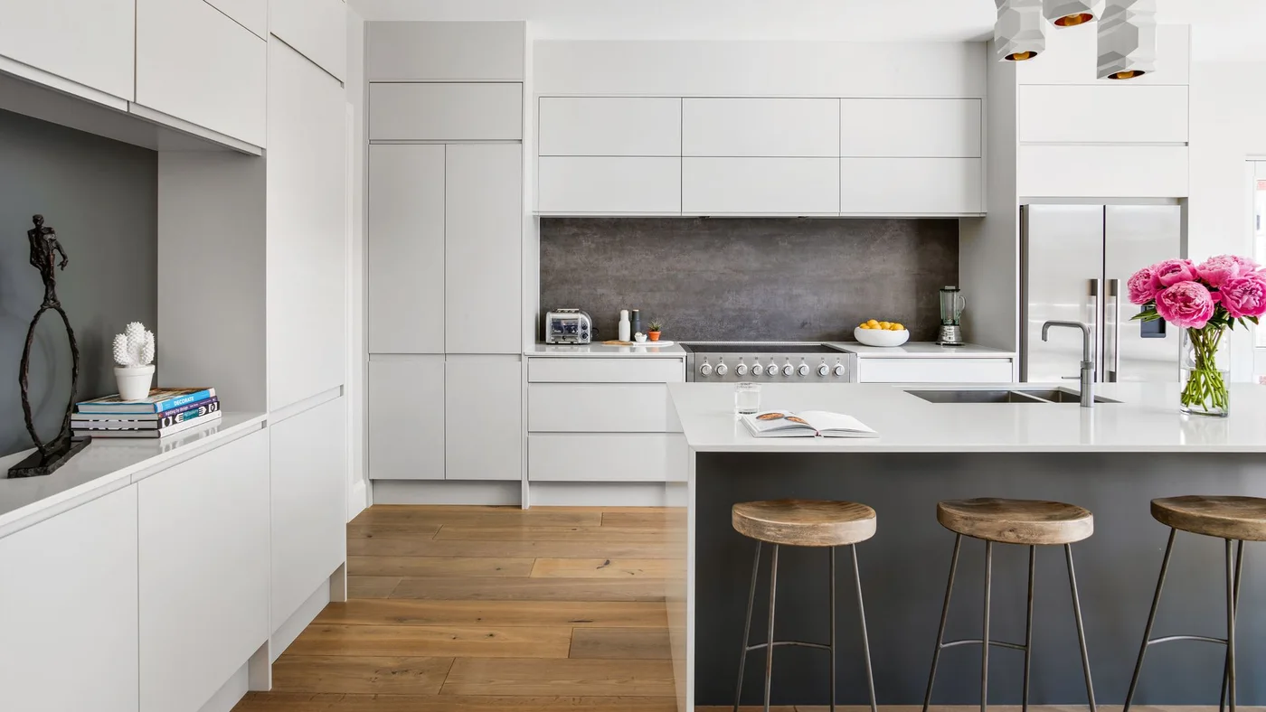 White flat-front cabinets surround a dark backsplash, a gray island and wooden stools