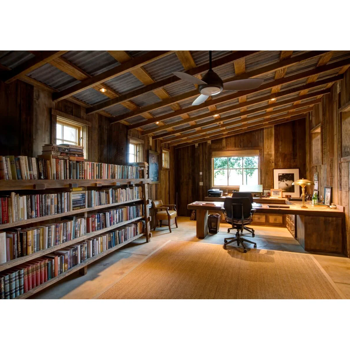 Wood-lined office with a long low bookcase, broad desk, dark office chair and pale woven rug