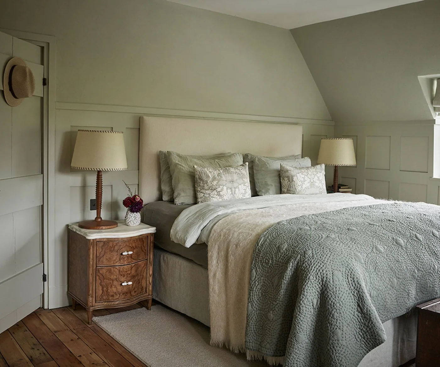 Gray-green painted bedroom walls, door and paneling with a pale headboard and green-gray bedding.