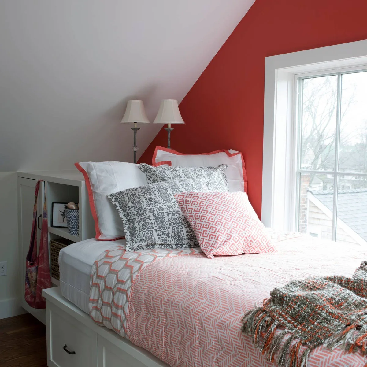 Single bed beneath an attic slope with a coral wall, white storage unit and under-bed drawer