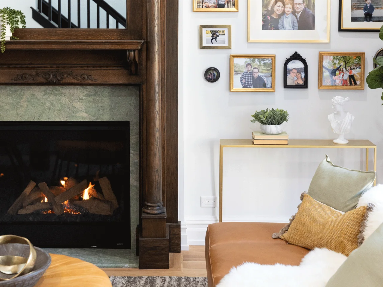 A tan sofa sits beside a dark carved timber fireplace and a wall of family photographs in mixed frames.