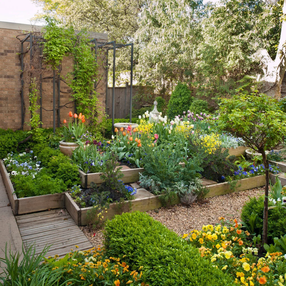 Rectangular timber beds at different levels hold colorful flowers beside narrow gravel and wood paths.