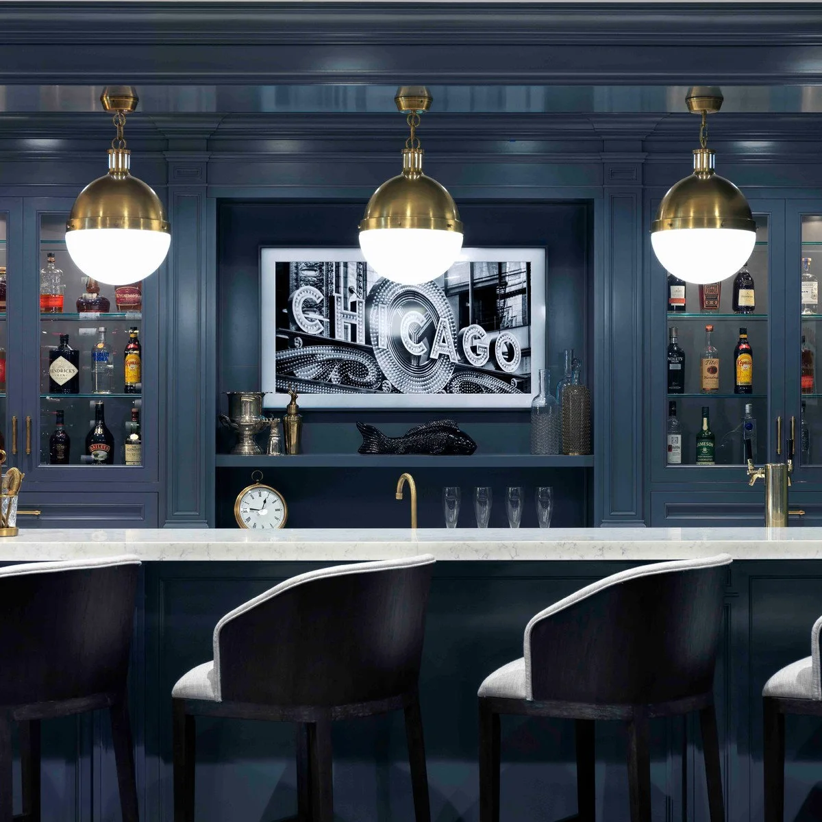 Deep blue home bar with glass-front cupboards, gold-colored pendants and pale counter