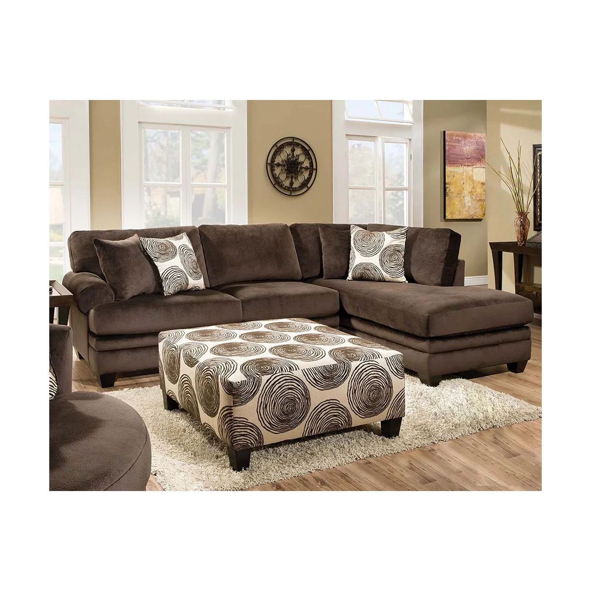 Chocolate brown fabric chaise sofa with a swirl-patterned ottoman and coordinating patterned cushions.