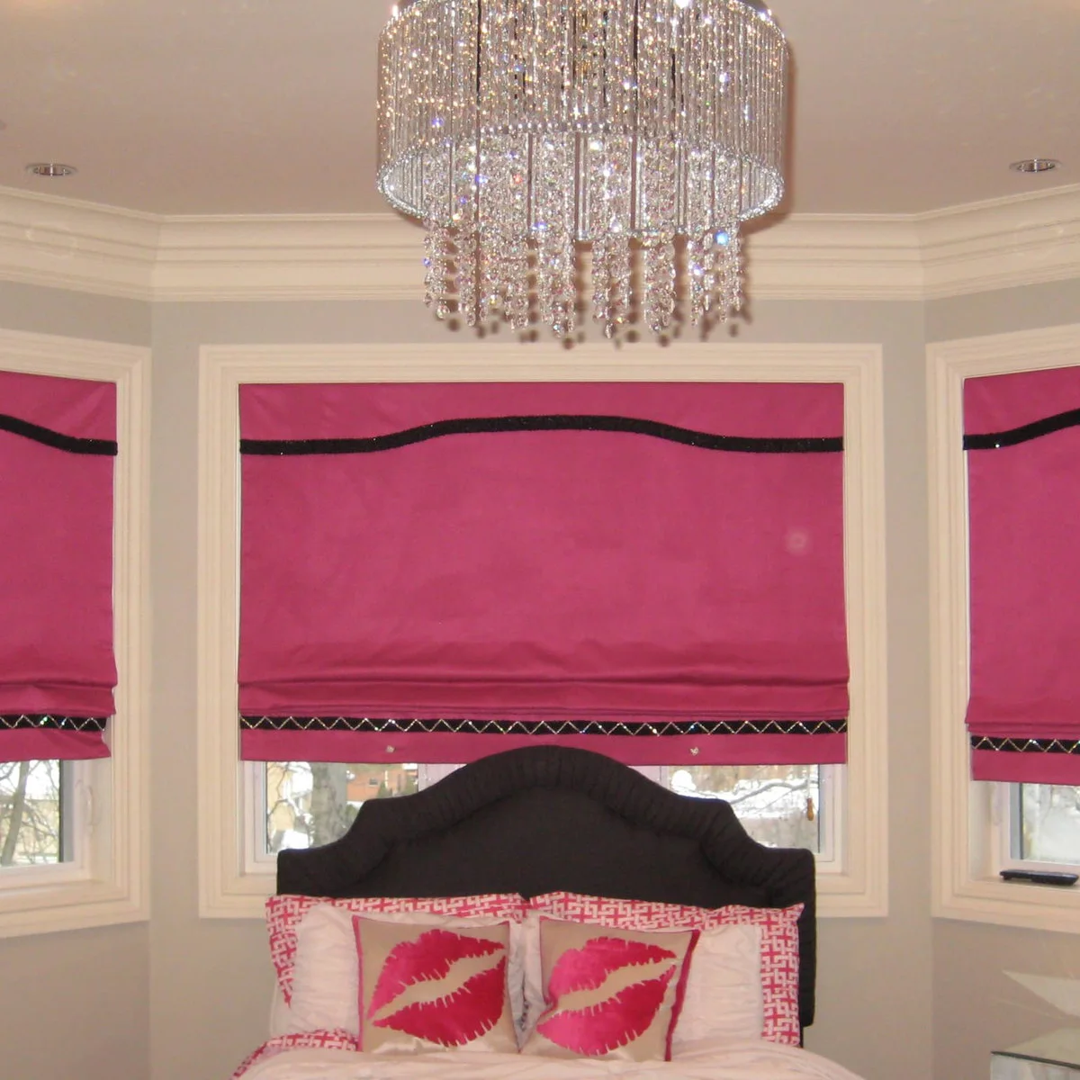Teen bedroom bay window with pink Roman blinds above a dark headboard and pink accent pillows