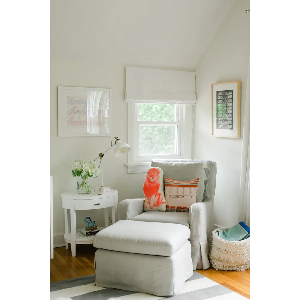 Pale nursery armchair with a large footstool, white side table and orange-accented cushions