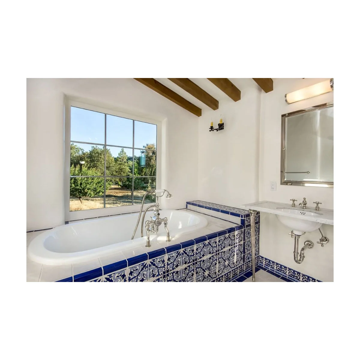 White bathroom with blue-and-white patterned tiles on a built-in bath apron and a wall-mounted basin