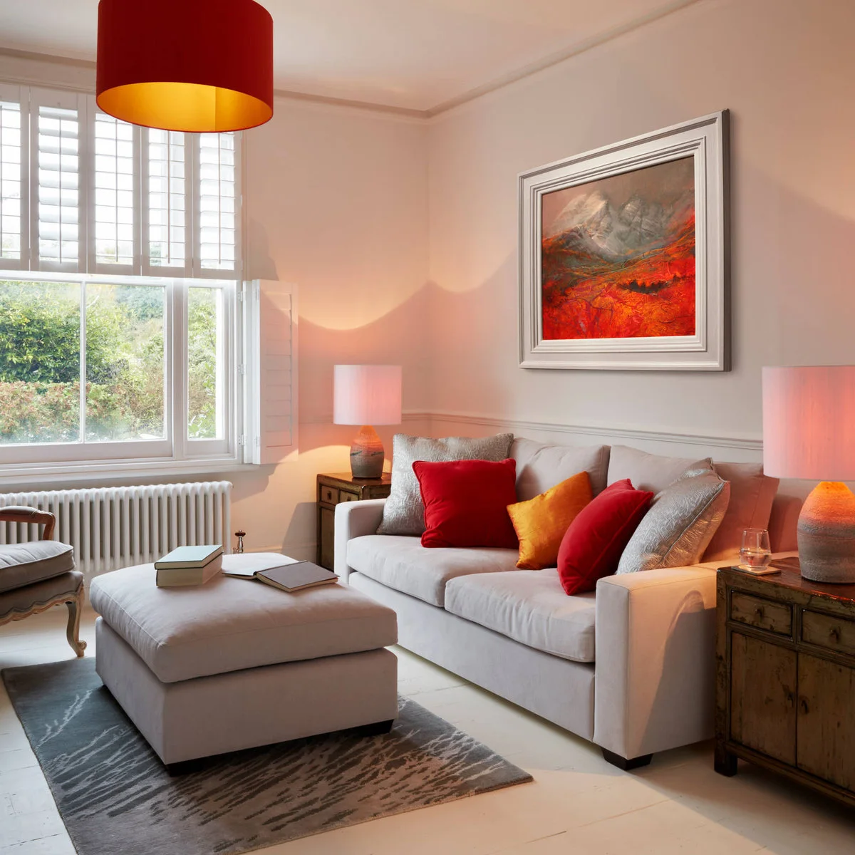 Pale sofa with red and yellow cushions, upholstered ottoman and matching lamps in an end-terrace room