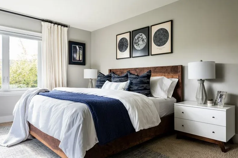 Bedroom with three framed celestial prints above a wood headboard, white bedding and a dark blue throw.