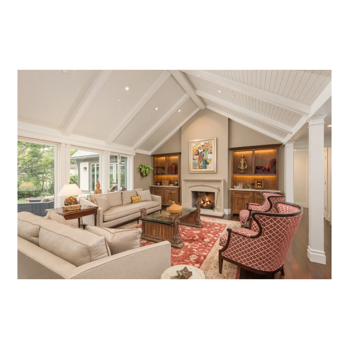 Vaulted living room with pale sofas, red patterned chairs and a fireplace between illuminated wood shelves