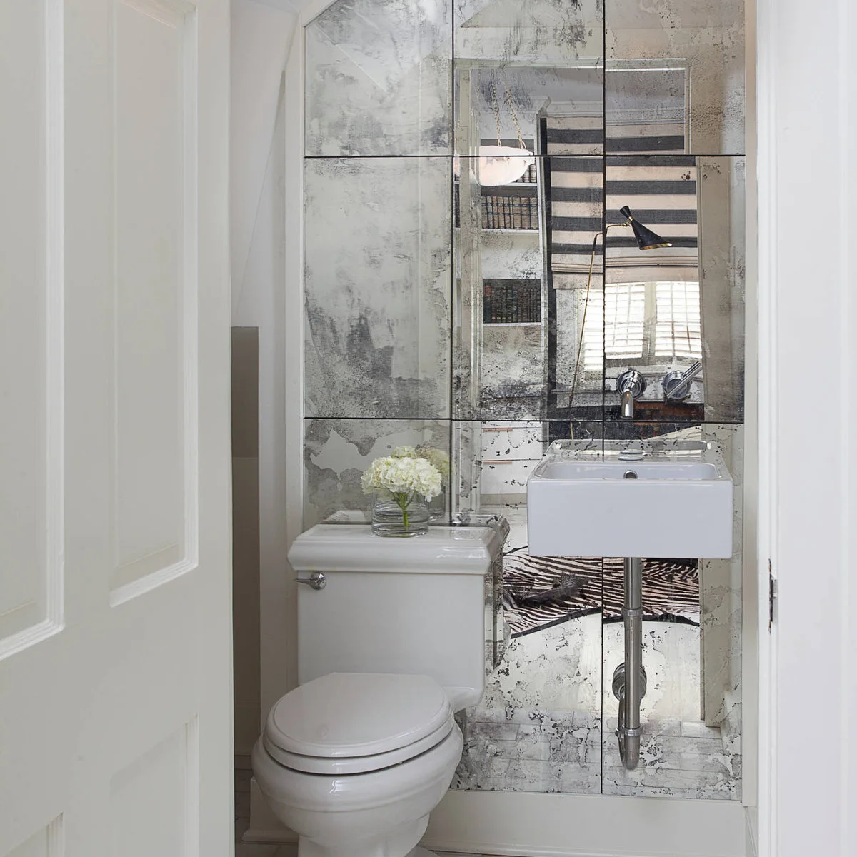 Distressed mirror panels behind a small wall-mounted powder-room sink