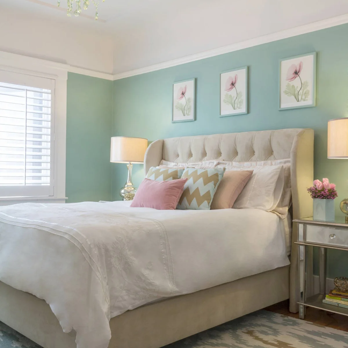 Mint bedroom wall behind a cream tufted headboard, pink chevron cushions and three pink botanical prints
