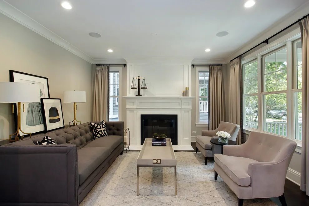 A dark gray sofa faces light chairs beside a fireplace and a large window
