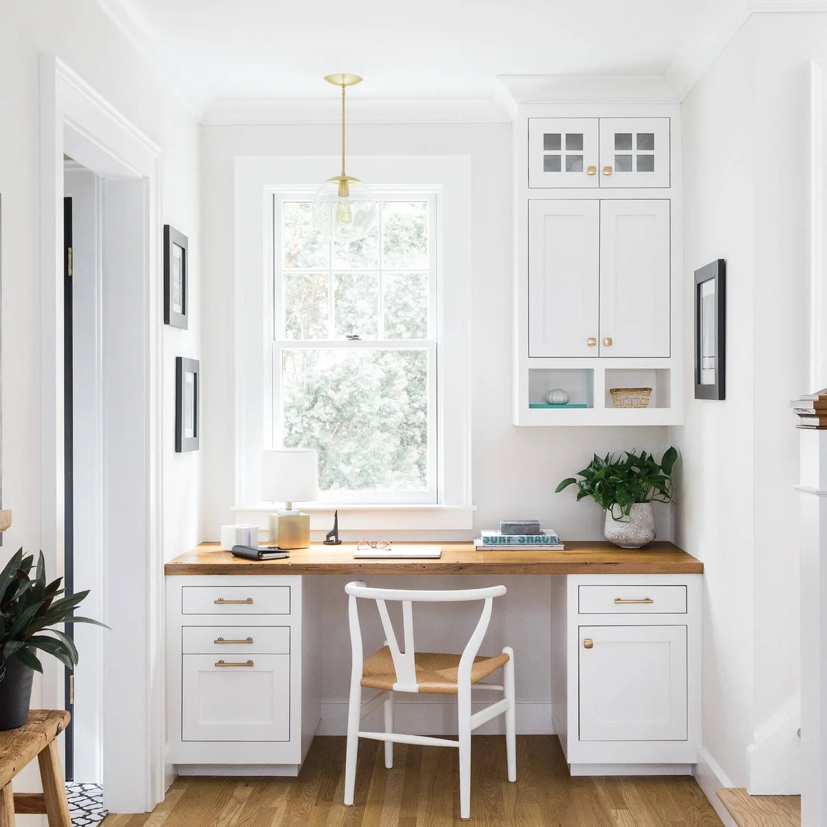 White built-in desk with wood top, drawers on both sides and a tall window above the seated opening