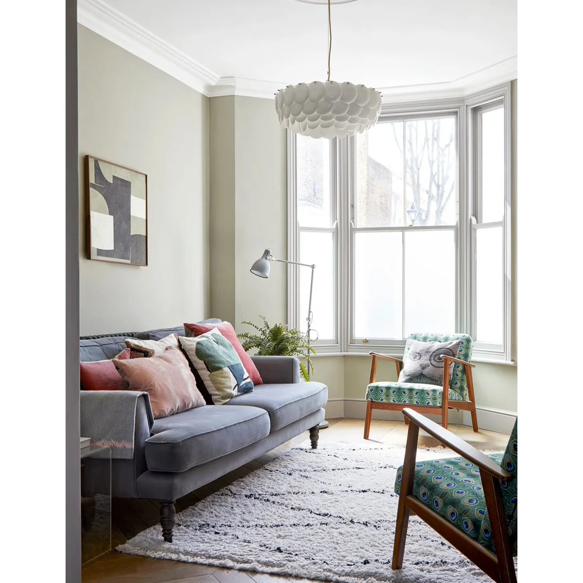 Gray sofa opposite wood-framed patterned chairs beneath a tall bay window