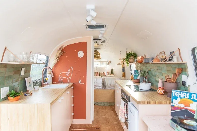 Pale green rectangular tiles line both sides of a compact galley kitchen beside pale counters and a curved coral partition