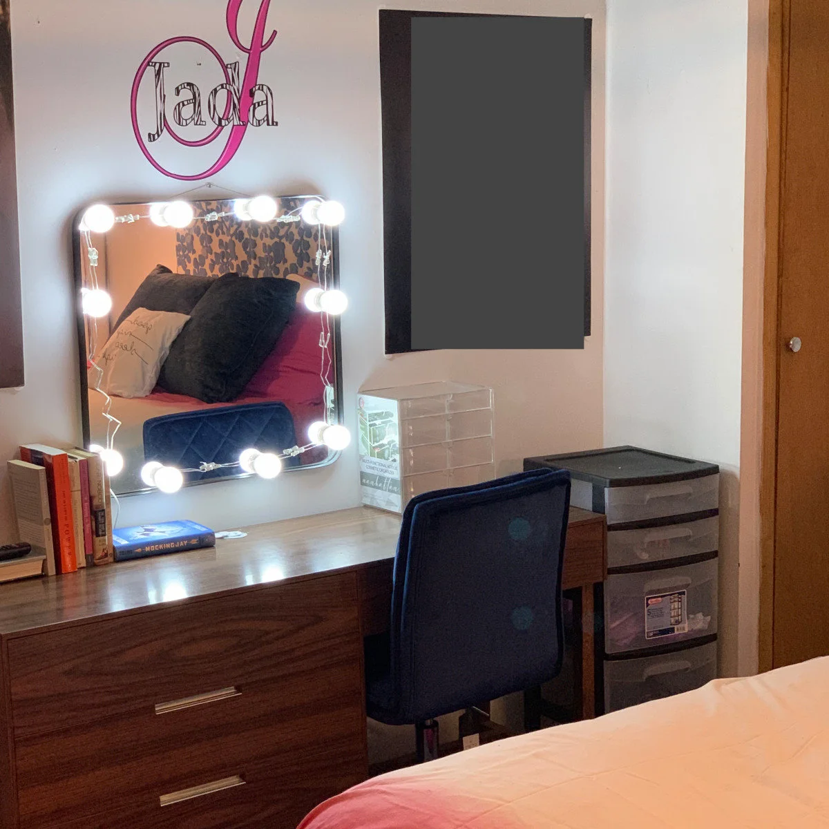 Wood student desk with a lighted mirror, books, navy chair and a separate plastic drawer unit