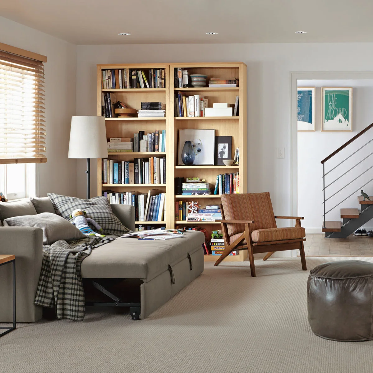 Gray sleeper sofa with an extended platform, visible support mechanism and pull tabs beside bookcases