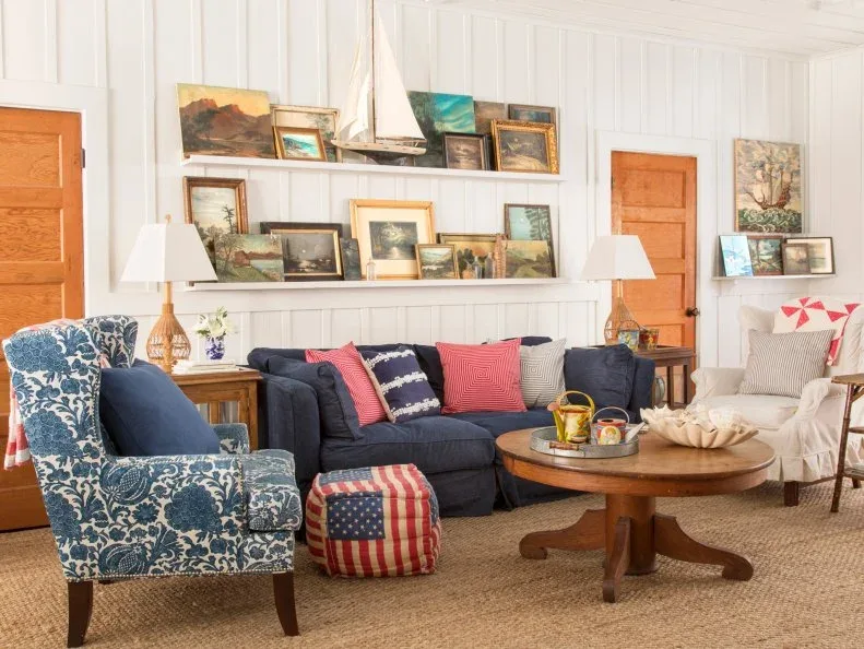 Navy sofa beneath picture shelves and a model sailboat, with a blue floral chair and round wooden table.