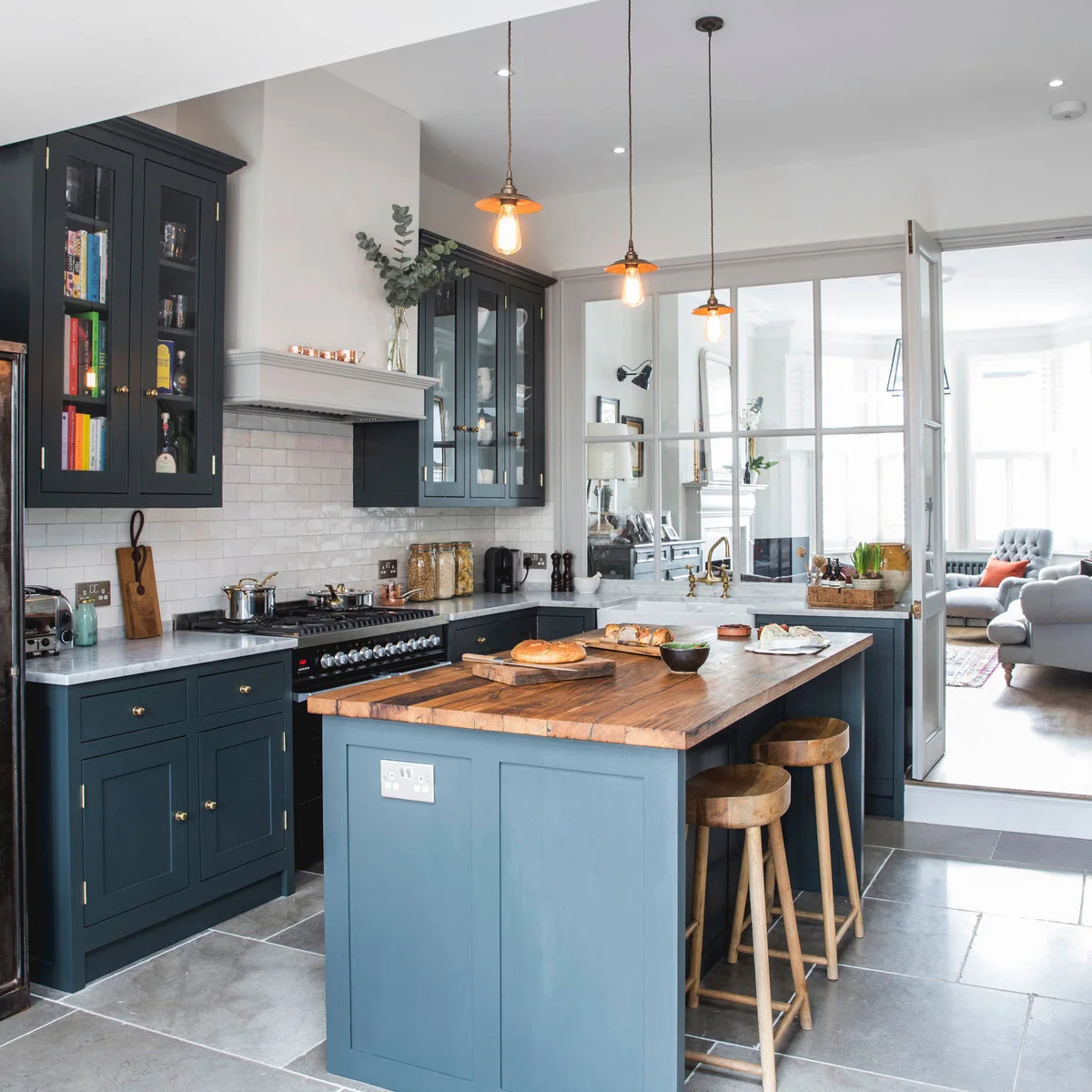 Dark green terrace-house kitchen with a wood-topped island and a glazed partition toward the sitting room