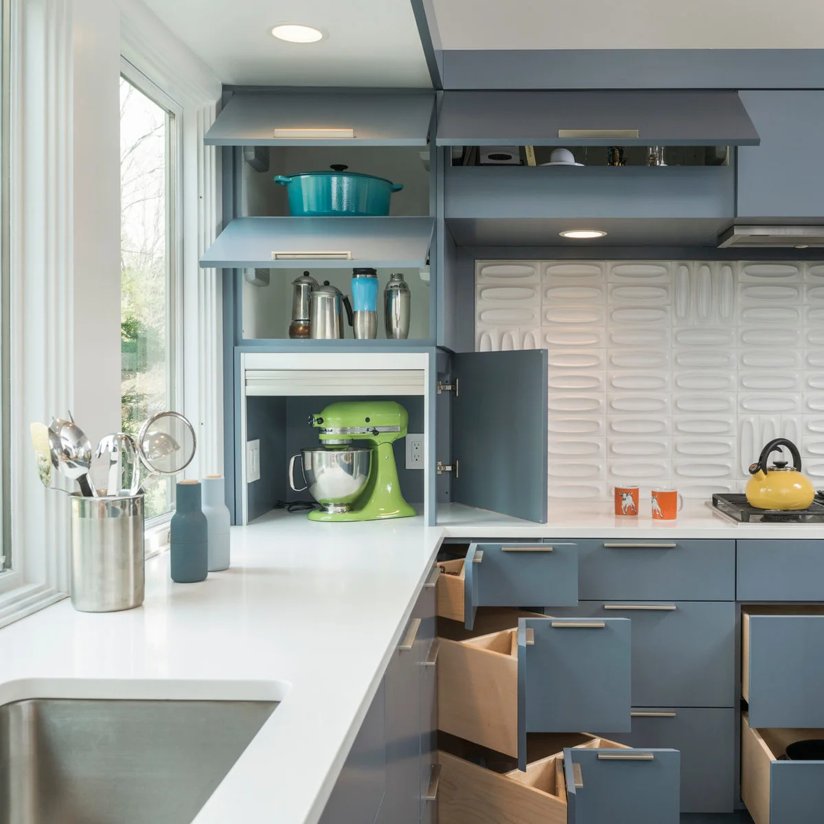 Blue kitchen with open angled corner drawers and a green mixer in an appliance cupboard